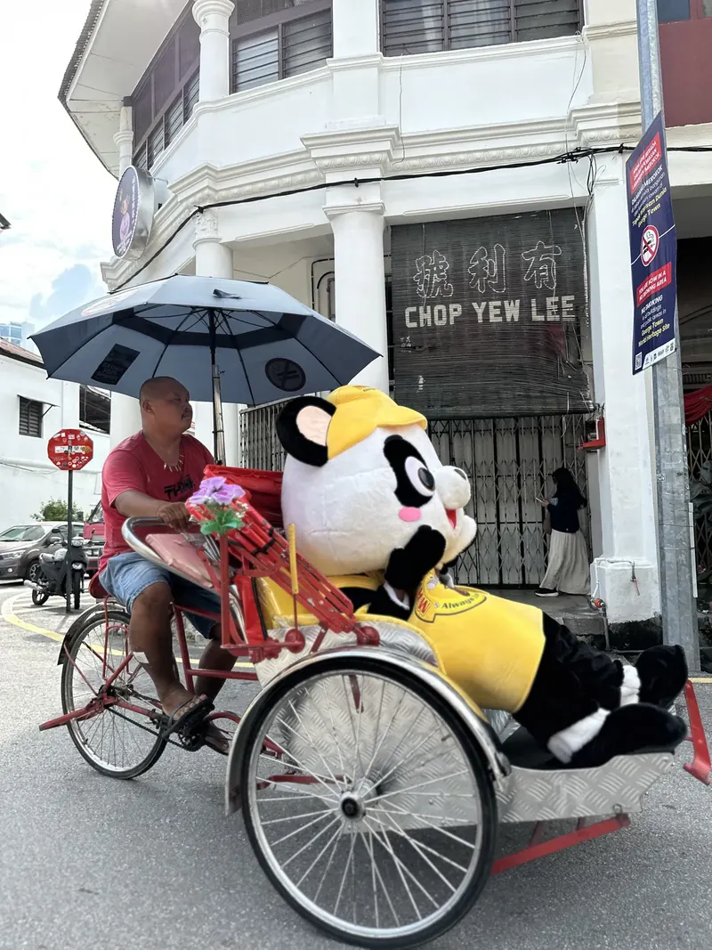 A PANDAi mascot riding a trishaw through the streets of Penang