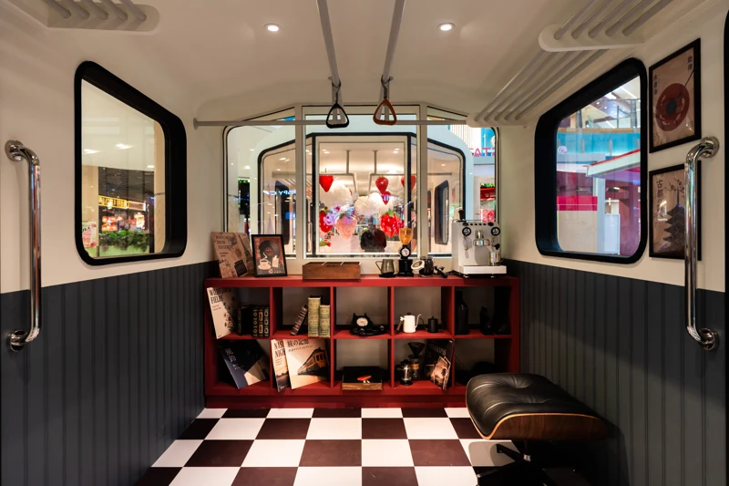 POKKA coffee cabin with a bean jar, coffee grinder and espresso machine on a red display shelf, alongside records, books, brewing accessories and upholstered seating.