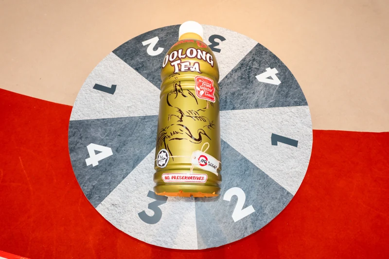 Overhead view of the oversized POKKA Oolong Tea bottle on the circular Spin the Bottle platform, numbered one to four