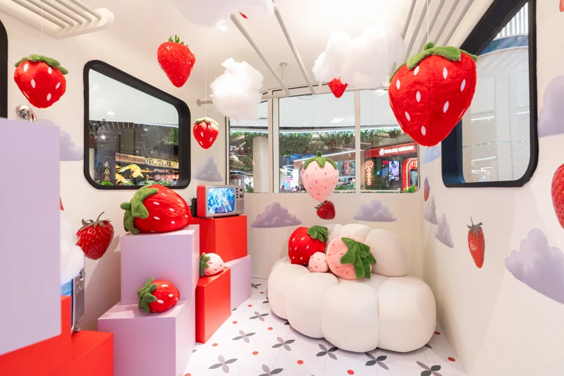 Interior of POKKA’s strawberry train cabin with hanging strawberries, soft clouds, a rounded white sofa and pastel display blocks.