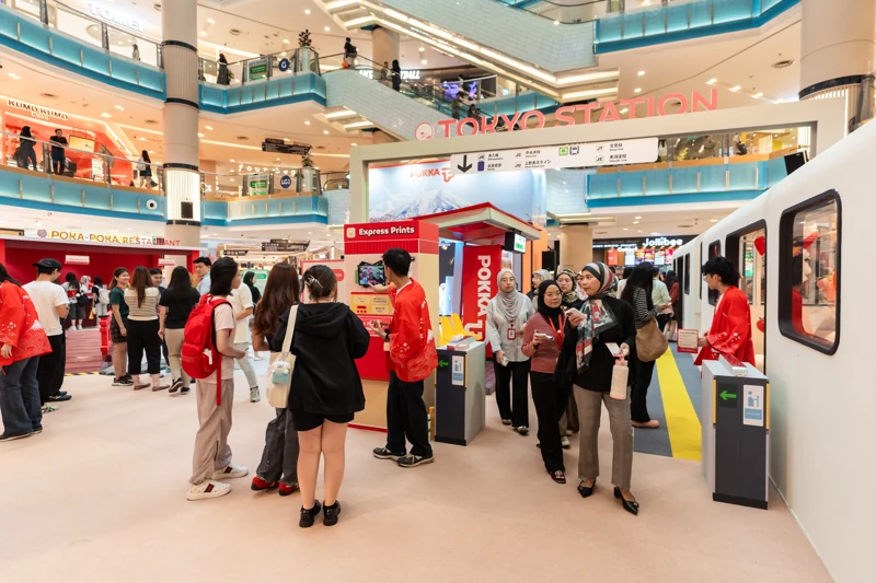 Guests and POKKA promoters beside Tokyo Station signage, the receipt photobooth and the train cabins.