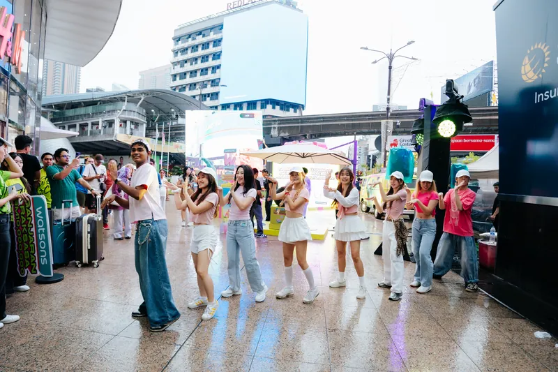 The afternoon flashmob: dancers in pink tops, white caps and denim dance in formation on a wet walkway outside Lot 10 while passers-by watch, 14 April 2026