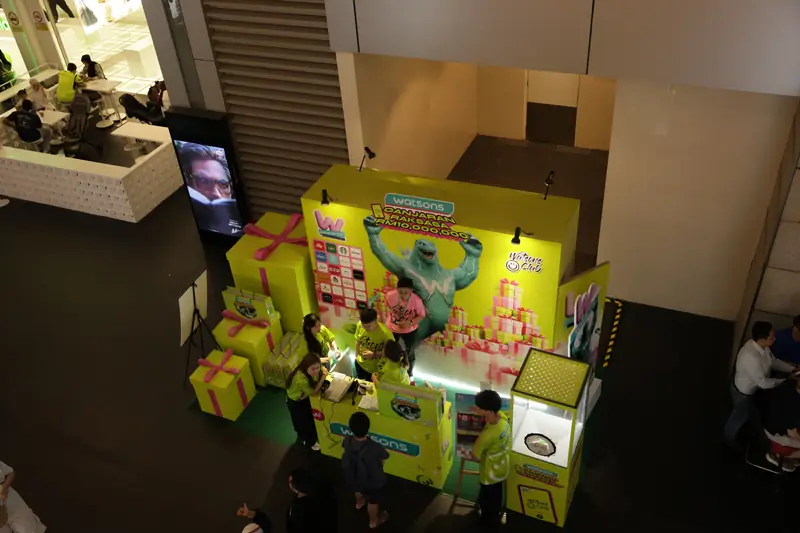 The Watsons redemption booth at Pavilion Kuala Lumpur’s Connection seen from above: monster backdrop, gift-box props, redemption counter, crew and the wrapped wind-chamber game, 19 April 2026