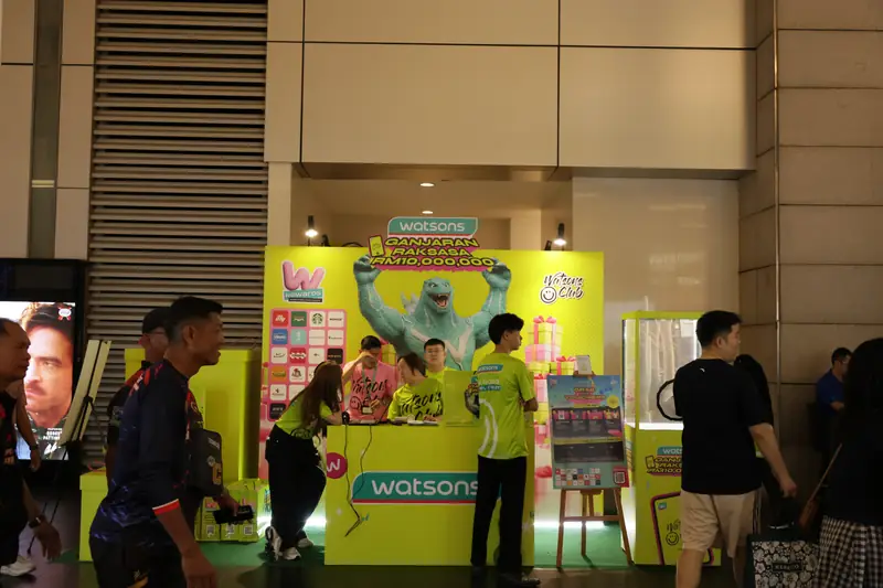 Crew working the redemption counter at Pavilion Kuala Lumpur on the final evening, with the wind-chamber game on the right, 19 April 2026