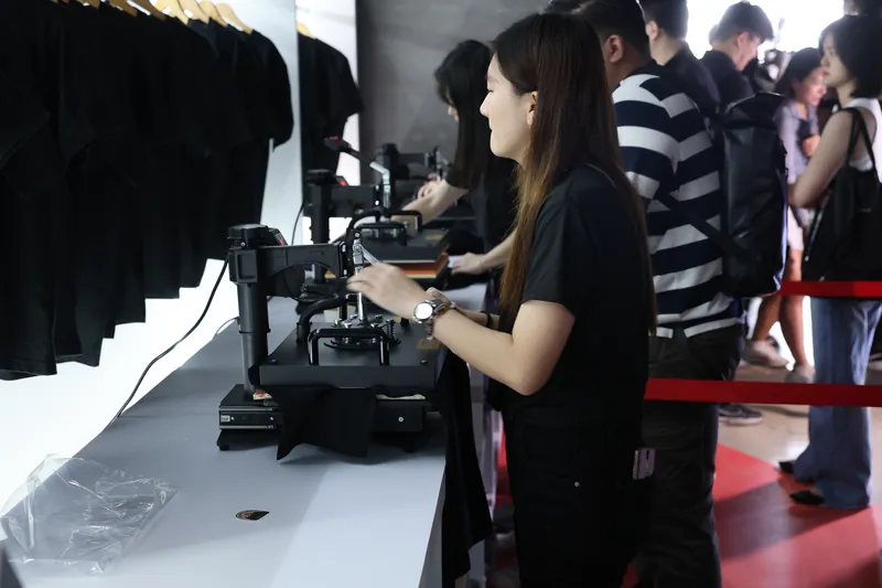 A Baito facilitator working a heat press at the X-perience Lab while guests queue behind a red rope, ZEEKR X launch, 23 June 2026