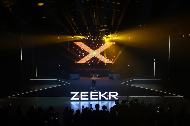 A pixel-art X fills the main LED wall above the two covered cars while the crowd films, ZEEKR X launch