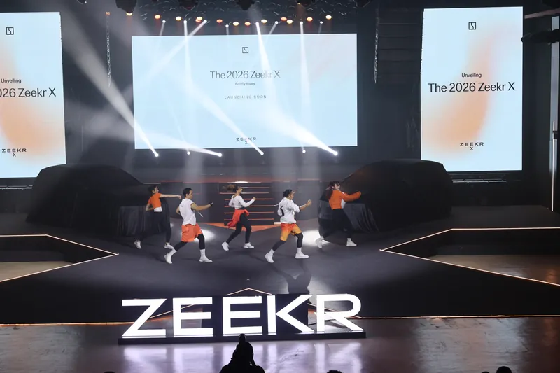 Five dancers performing in front of two covered ZEEKR X units on the launch stage, a lit ZEEKR wordmark in front