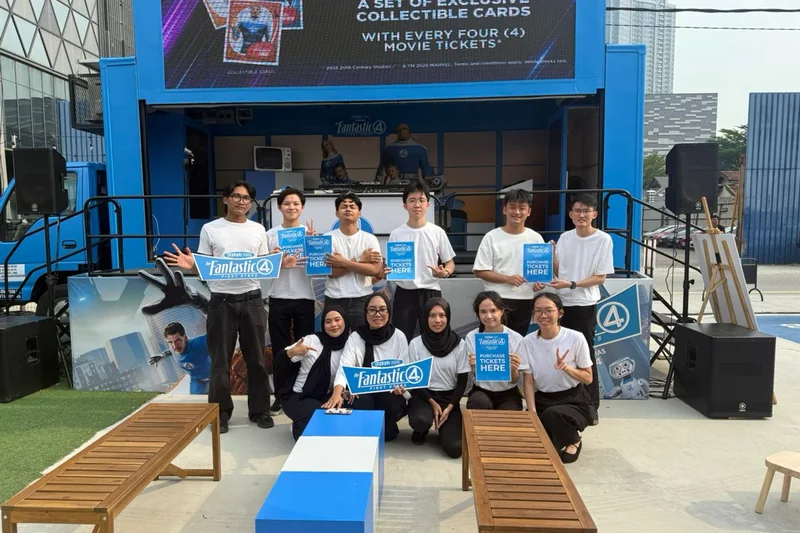 Eleven crew members in white tees in front of the stage truck at Pingmin Hub, holding Fantastic Four: First Steps placards and ‘Purchase tickets here’ boards, under the LED screen.