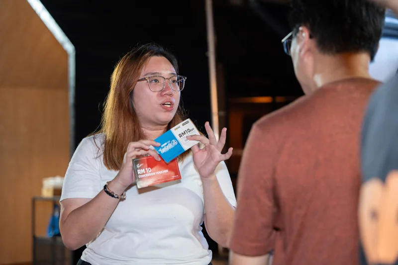 A crew member shows a guest two Fantastic Four-branded RM10 cinema vouchers.