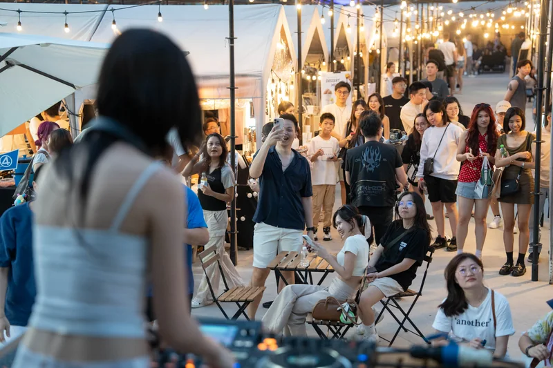 The DJ plays from the truck deck as a crowd gathers and sits on folding chairs at the night market, under festoon lights.