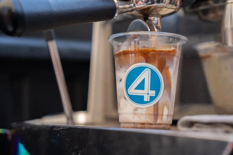 An espresso shot pours into a cup of milk carrying a Fantastic Four ‘4’ sticker.