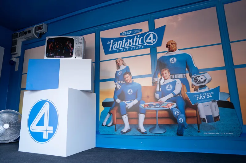 Inside the wrapped truck: a retro set with a Fantastic Four: First Steps backdrop of the four heroes on a sofa, a vintage TV on white cubes and a large ‘4’ cube.
