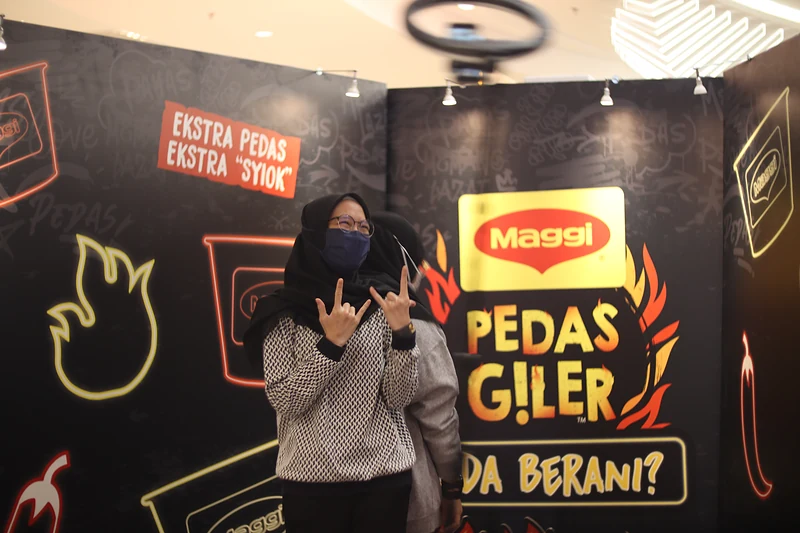 A masked guest strikes a pose on the 360 booth in front of the MAGGI Pedas Giler ‘Ada Berani?’ backdrop, the ring light circling overhead.