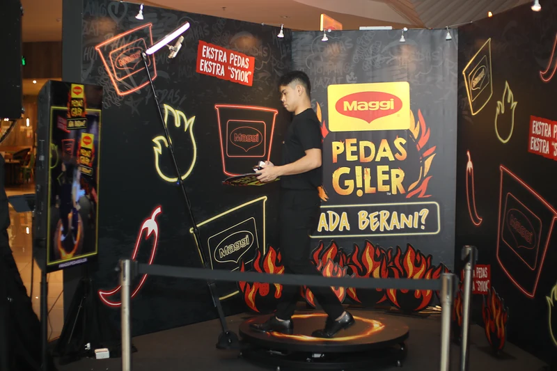 The 360 booth on the first morning: a round platform ringed with flames under an overhead rotating arm, in front of a MAGGI Pedas Giler ‘Ada Berani?’ backdrop and ‘Ekstra pedas, ekstra syiok’ signs.