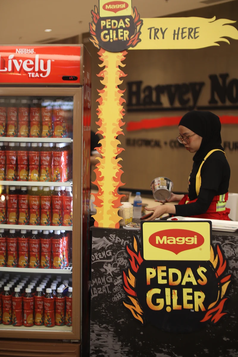 A team member in the campaign uniform works at the MAGGI Pedas Giler ‘Try here’ counter, next to a fridge of Nestlé Lively tea.