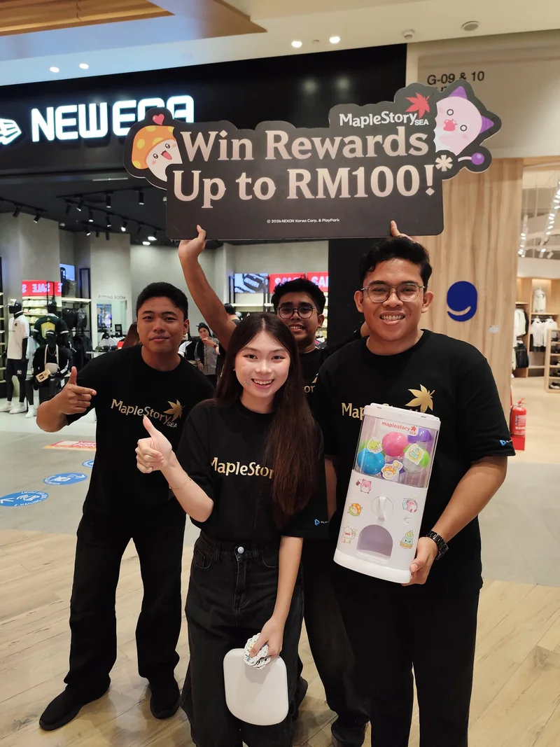 Four crew in MapleStorySEA tees under a ‘Win Rewards Up to RM100!’ sign; one holds a portable MapleStorySEA capsule machine filled with coloured capsules.