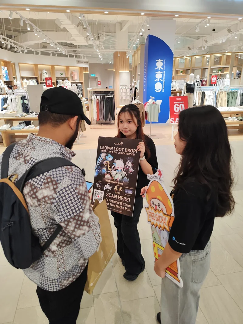 A crew member holds up the Crown Loot Drop poster for a shopper while another crew member holds a ‘FREE GACHA!’ cut-out.