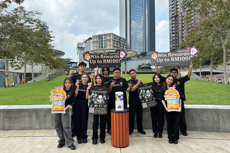 Crew in MapleStorySEA tees line up on LaLaport’s outdoor lawn with reward signs, Crown Loot Drop posters, ‘FREE GACHA!’ cut-outs and a MapleStorySEA capsule machine on a stand.
