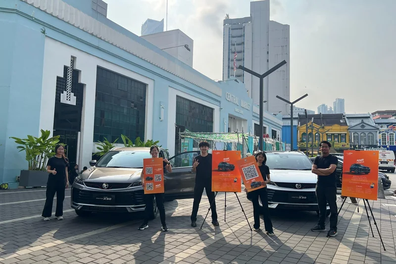 Baito crew in black tees hold orange Roar of Amazement boards beside two X50s outside Central Market, Kuala Lumpur
