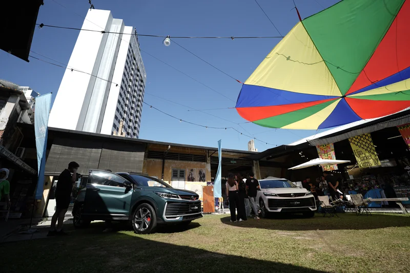 A dark and a white X50 on the lawn at Hin Bus Depot, George Town, under a striped canopy, with a tower block behind