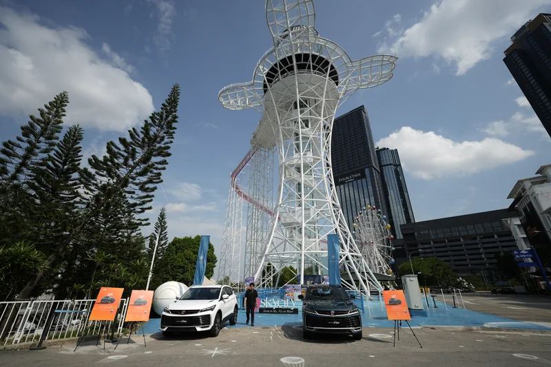 A white and a dark X50 parked by orange boards below the white i-City tower ride in Shah Alam, with the ferris wheel to the right
