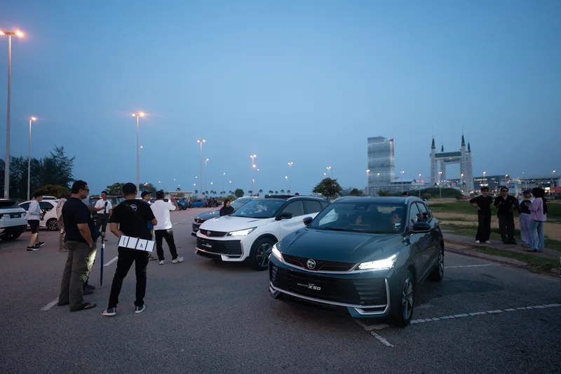 X50s with their headlights on at dusk in Kuala Terengganu, with people around them and the drawbridge on the skyline