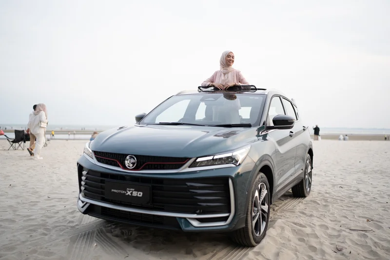 A woman leans out of the sunroof of a dark X50 parked on the sand at Teluk Cempedak, Kuantan