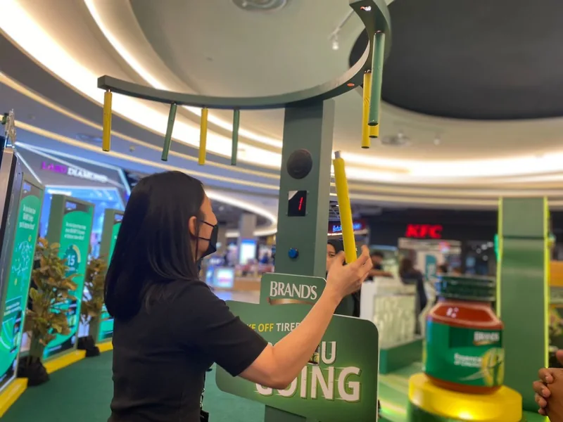The same stick-catching game unit at a different event, a BRAND’S activation: a participant catches a falling yellow stick beneath the green overhead ring